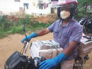 A civic-minded newspaper vendor in Tamil Nadu, India, wearing safety gloves, mask and safety screen