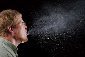 A man mid-sneeze. Original CDC caption: &quot;This 2009 photograph captured a sneeze in progress, revealing the plume of salivary droplets as they are expelled in a large cone-shaped array from this man’s open mouth, thereby dramatically illustrating the reason one needs to cover his/her mouth when coughing, or sneezing, in order to protect others from germ exposure.&quot;